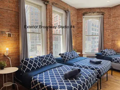 a bedroom with two beds and a couch and windows at NYC Empire Apartments in New York