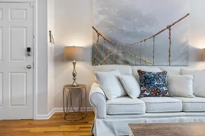 a living room with a white couch and a bridge painting at Close to NYC | King Bed | Free Parking in Bloomfield