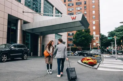 a man and woman standing in front of a building with a suitcase at W Hoboken in Hoboken