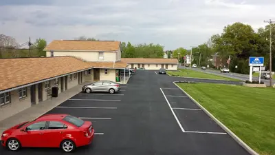 a red car parked in a parking lot next to a building at Americas Best Value Inn - Palmyra/Hershey in Palmyra