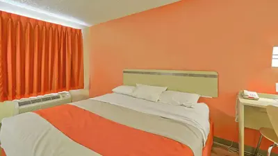a bedroom with an orange wall with a bed and a desk at Motel 6-Maple Shade Township, NJ - Philadelphia - Mt Laurel in Maple Shade