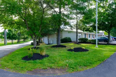 a green lawn with trees in front of a building at American Inn in Carlisle