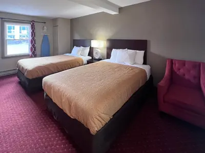 a hotel room with two beds and a red chair at Rodeway Inn & Suites Hershey Chocolate Avenue in Hershey