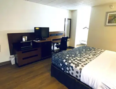 a bedroom with a bed and a desk with a television at Travelodge by Wyndham Shamokin Dam/Selinsgrove in Shamokin Dam