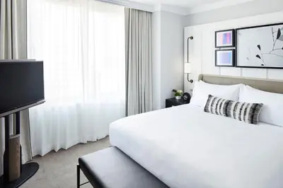 a white hotel room with a bed and a tv at The Luxury Collection Hotel Manhattan Midtown in New York