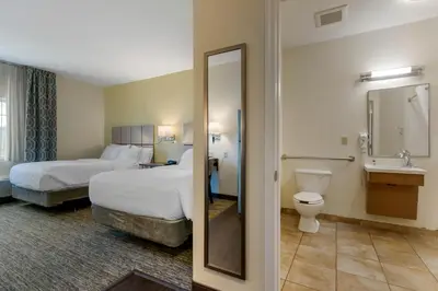 a hotel room with two beds and a bathroom with a mirror at Candlewood Suites Reading by IHG in Reading