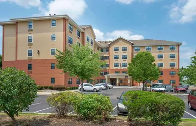 an apartment building with cars parked in a parking lot at Extended Stay America Suites - Secaucus - Meadowlands in Secaucus