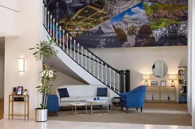 a lobby with a staircase with a couch and chairs at Penn Harris Hotel Harrisburg, Trademark by Wyndham in Harrisburg
