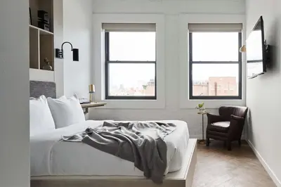 a bedroom with a bed and a chair and two windows at Walker Hotel Tribeca in New York