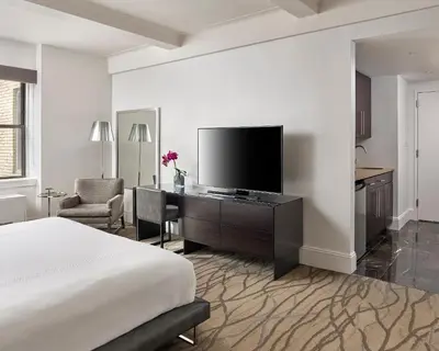a bedroom with a bed and a desk with a television at AKA Central Park in New York