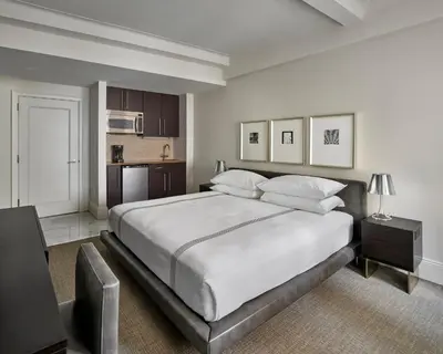 a bedroom with a large white bed and a kitchen at AKA Central Park in New York