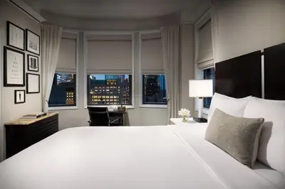 a bedroom with a large white bed with a desk and windows at The Gregorian New York City in New York