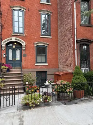 a building with a fence and flowers in front of it at Historic 1869 Brownstone 15 min to NYC downtown in Jersey City