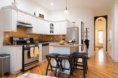 a kitchen with white cabinets and a island with bar stools at Historic 1869 Brownstone 15 min to NYC downtown in Jersey City