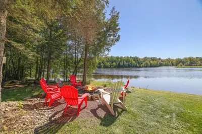 a group of chairs sitting around a fire next to a lake at Mt. Maplewood Lake House in Blakeslee