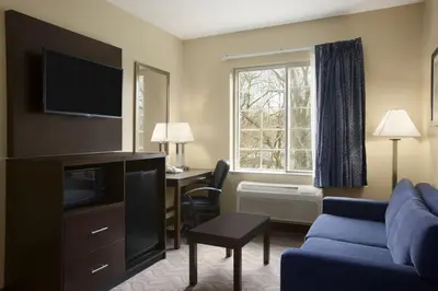 a hotel room with a couch and a desk and a window at Days Inn & Suites by Wyndham Cherry Hill - Philadelphia in Cherry Hill