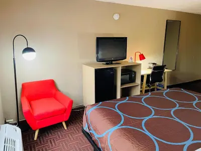 a hotel room with a bed and a red chair and a television at Super 8 by Wyndham Gloucester in Gloucester City