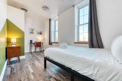 a bedroom with a bed and a desk and windows at The Stairway Suites - Convention Center in Philadelphia