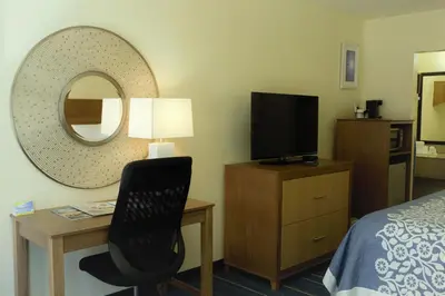 a hotel room with a desk and a chair and a mirror at Days Inn by Wyndham Newark Wilmington in Newark