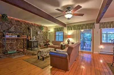 a living room with a stone wall and a ceiling fan at 1 Mi to Lake Wallenpaupack Pocono Mountain Home! in Greentown