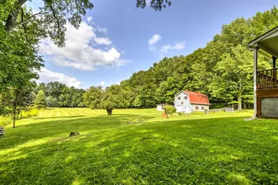 a grassy field with a house and a barn at Thompson Home with Deck and Pond, 8 Mi to Elk Mountain in Thompson