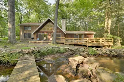 a log cabin in the woods next to a river at Secluded Stroudsburg Home - 5 Mi to Ski Resort in Stroudsburg