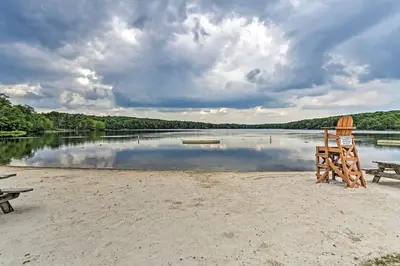 a beach with two chairs and a bench and a lake at Pocono Mountain Home with 3 Community Lakes! in Gouldsboro