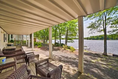 a porch with chairs and tables and a view of a lake at Waterfront Pocono Lake Home with Private Dock! in Pocono Lake