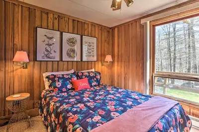 a bedroom with a bed with a blue comforter and a window at Walk to Big Bass Lake Family Home with Deck! in Gouldsboro