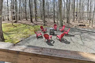 a group of red chairs and a table in the woods at Walk to Big Bass Lake Family Home with Deck! in Gouldsboro
