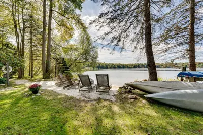 a group of chairs and a boat on the side of a lake at Luxe Poconos Pines Home with Beach and Amenities! in Pocono Pines