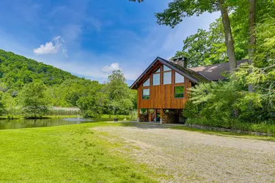 a barn style house with a river and trees at Secluded Cabin with Boats Less Than 6 Mi to Jenny Jump! in Great Meadows