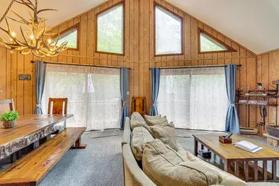 a living room with couches and a table and windows at Fire Pit and Games! Secluded Chalet 30 Mi to Montage in Lake Ariel