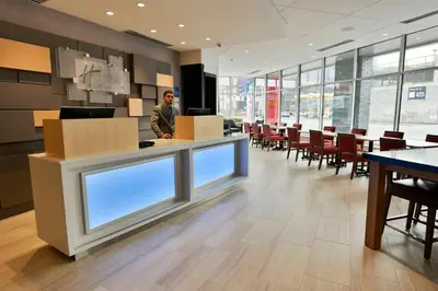 a man standing at a counter in a room with tables and chairs at Holiday Inn Express & Suites Jersey City - Holland Tunnel by IHG in Jersey City