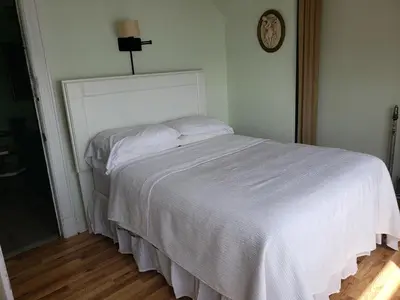 a white bed in a bedroom with a clock on the wall at Harbor House Bed and Breakfast in Staten Island