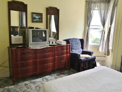 a bedroom with a dresser with a tv and a chair at Harbor House Bed and Breakfast in Staten Island