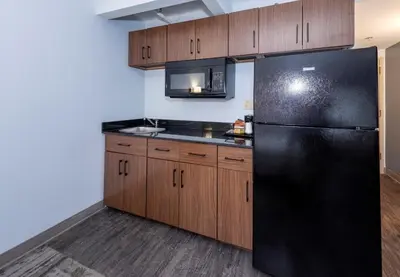 a kitchen with a black refrigerator and wooden cabinets at HomeTowne Studios by Red Roof Wilmington - New Castle in New Castle