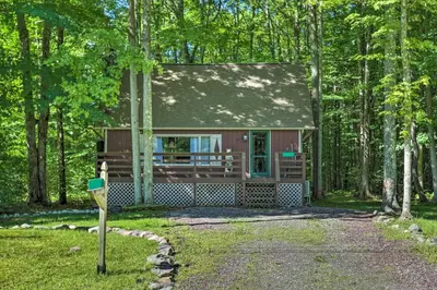 a small house in the woods with a driveway at Quaint Lake Cottage with Pool and Beach Access! in Pocono Lake
