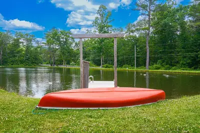 a red boat sitting on the grass near a body of water at Close to Slopes Lakeside Cottage in Pocono Mtns in Brodheadsville