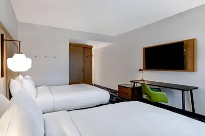 a hotel room with two beds and a green chair at Fairfield Inn & Suites by Marriott Selinsgrove in Selinsgrove
