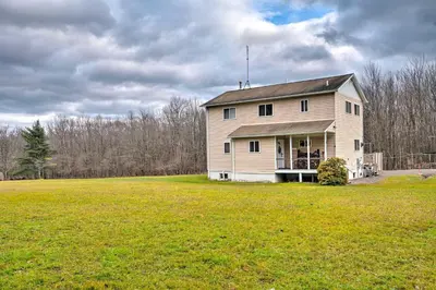 a large white house in a field with a grass yard at Private Hot Tub and Fireplace Poconos Home! in Pleasant Mount