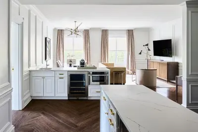 a kitchen with white cabinets and a living room at The Chateau Grande Hotel in East Brunswick
