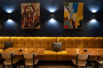 a yellow couch in a restaurant with two tables and paintings at Holiday Inn Lancaster by IHG in Lancaster