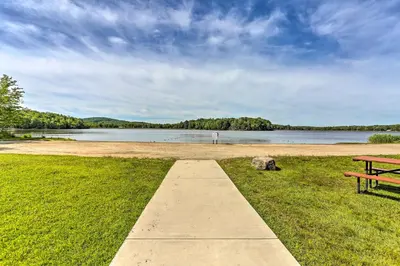 a park bench sitting on the grass next to a lake at Excellent Lakeview Getaway with Watercrafts Included in Pocono Lake