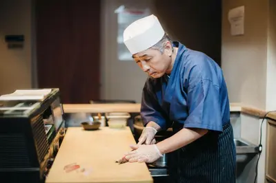 a man in a chefs hat standing in a kitchen preparing food at Henn na Hotel New York in New York
