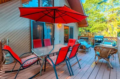 a table and chairs with a red umbrella on a deck at 3 Mi to Slopes! Poconos Chalet with Hot Tub and Sauna in Lake Harmony