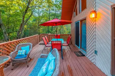 a deck with a table and chairs and an umbrella at 3 Mi to Slopes! Poconos Chalet with Hot Tub and Sauna in Lake Harmony