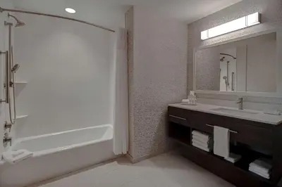 a bathroom with a tub and a sink and a mirror at Home2 Suites East Hanover, NJ in East Hanover