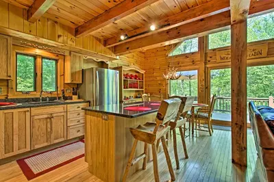 a kitchen with wooden cabinets and a counter with chairs at Fire Pit and Hot Tub Poconos Family Cabin! in Long Pond