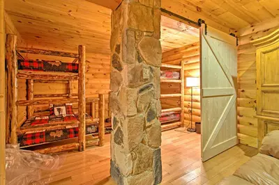 a log cabin bedroom with two bunk beds and a stone pillar at Fire Pit and Hot Tub Poconos Family Cabin! in Long Pond